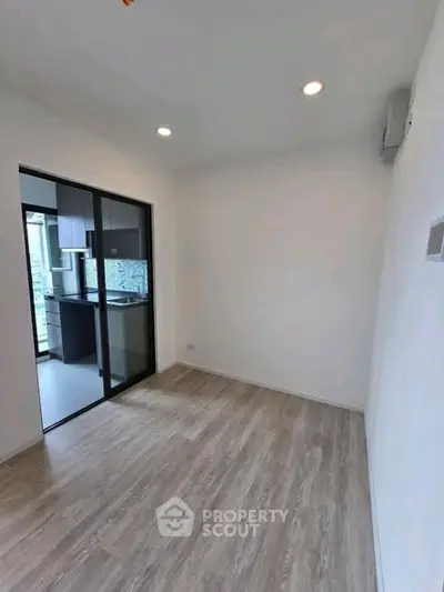 Modern empty room with wooden flooring and glass door to kitchen