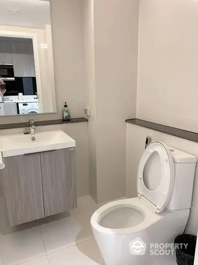 Modern bathroom with sleek finishes, featuring a floating vanity unit and a large mirror, reflecting a hint of the adjacent kitchen area.