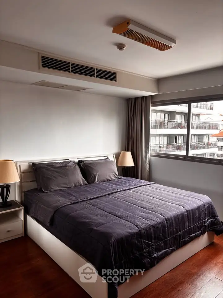 Spacious bedroom with modern decor and large window offering city views, perfect for urban living.