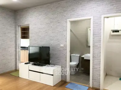 Modern apartment with open living area and bathroom access, featuring stylish brick walls.