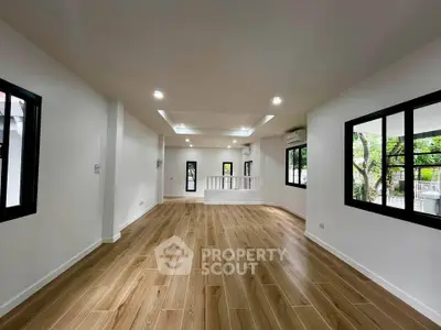 Spacious modern living room with wooden flooring and large windows offering natural light.