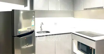 Modern kitchen with sleek appliances and minimalist design, featuring a fridge, sink, and electric stove.