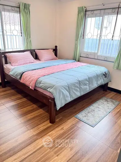 Cozy bedroom with wooden flooring and large windows, featuring a comfortable double bed and pastel bedding.