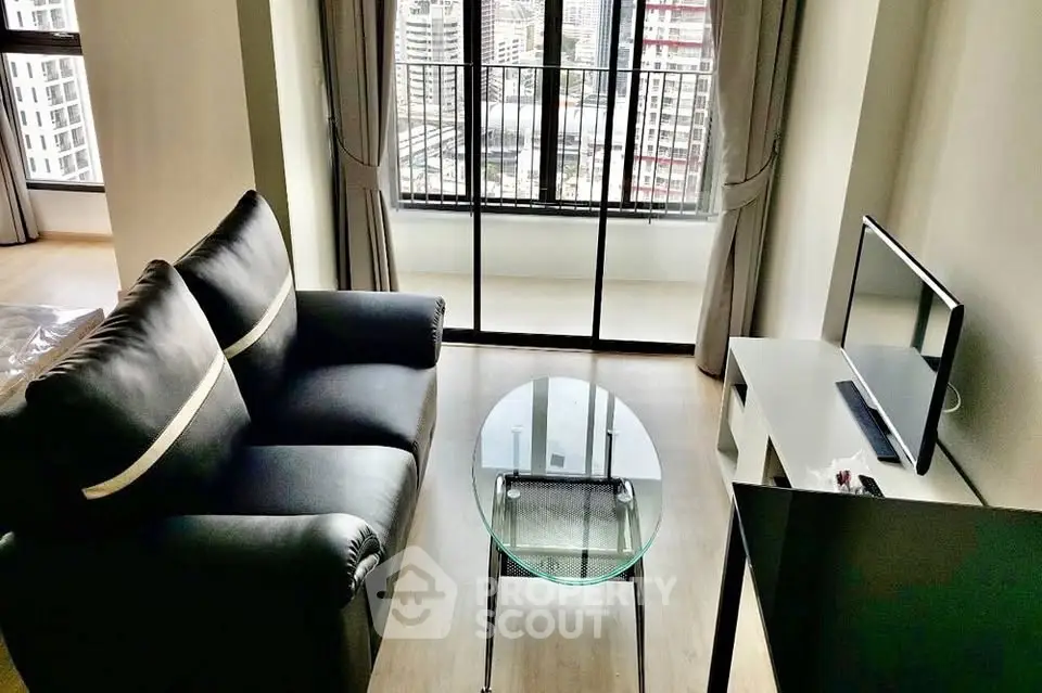 Modern living room with sleek black sofa and glass coffee table, featuring a city view from large windows.
