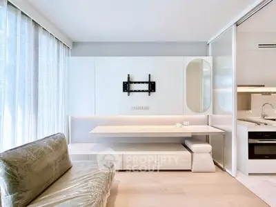 Modern living room with sleek furniture and built-in kitchen appliances in a bright, minimalist apartment.