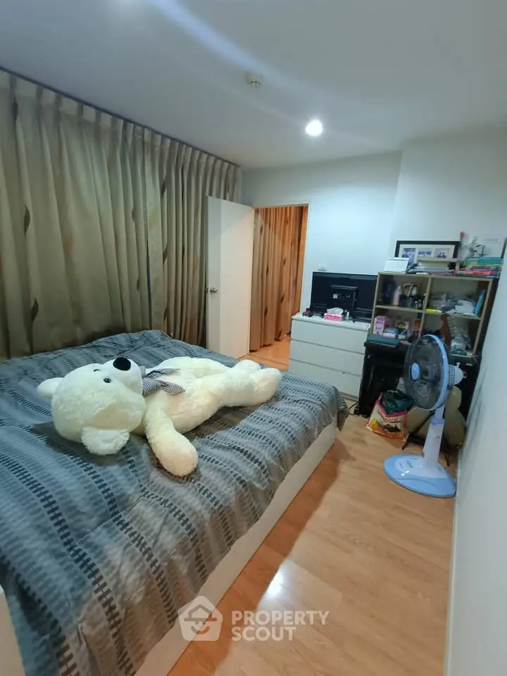 Cozy bedroom with wooden flooring, large teddy bear on bed, and organized shelving.