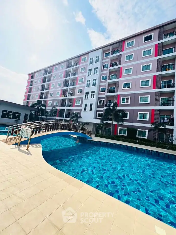 Modern apartment building with a large swimming pool and sunny sky view.