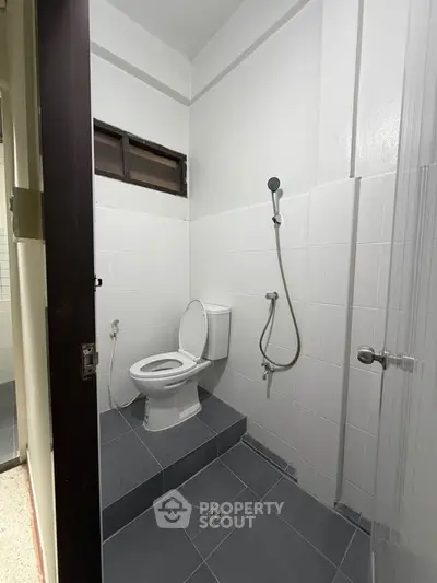 Compact bathroom with elevated toilet and shower area in modern apartment.