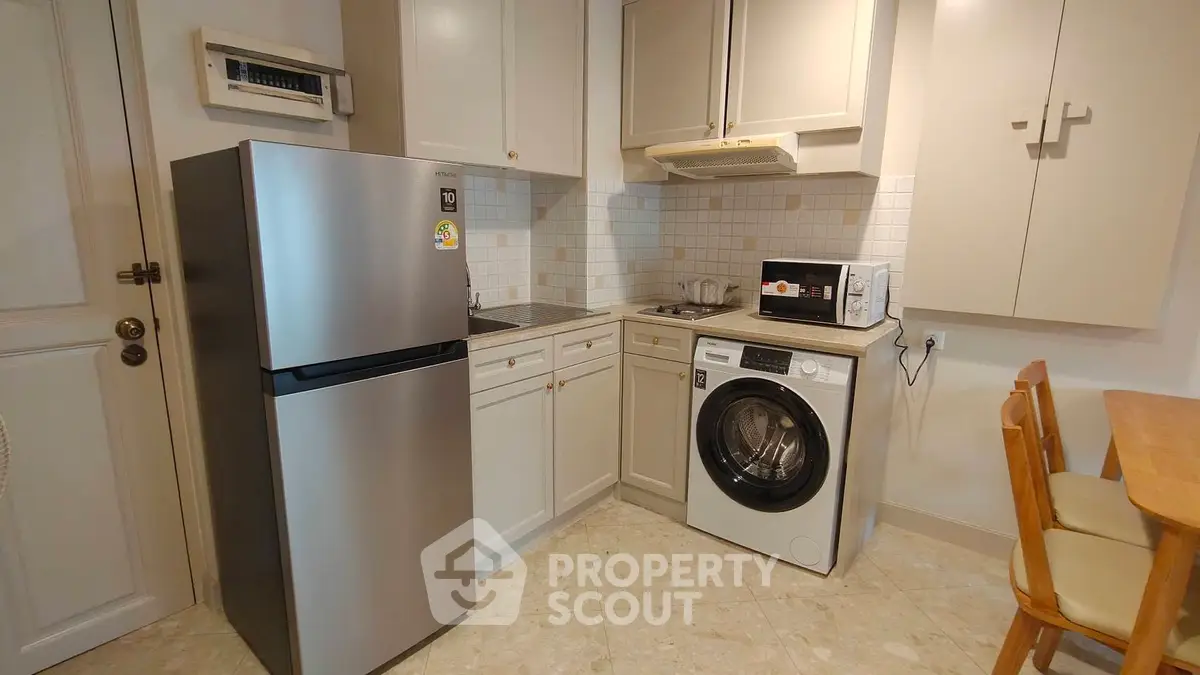 Modern kitchen with stainless steel fridge, washing machine, and microwave in cozy apartment.