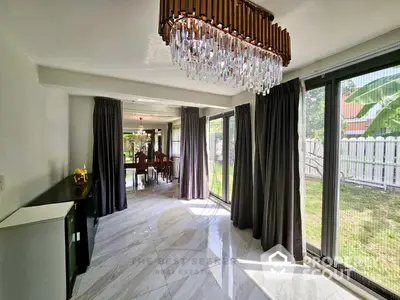 Elegant living space with gleaming marble floors and a luxurious crystal chandelier, leading to a lush garden view through floor-to-ceiling windows.