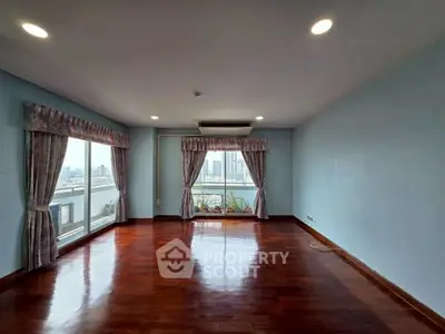 Spacious living room with large windows and city view, featuring elegant curtains and polished wooden floors.