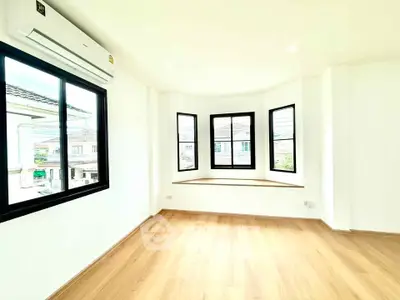 Bright and airy room with large windows and wooden flooring, perfect for a cozy living space.