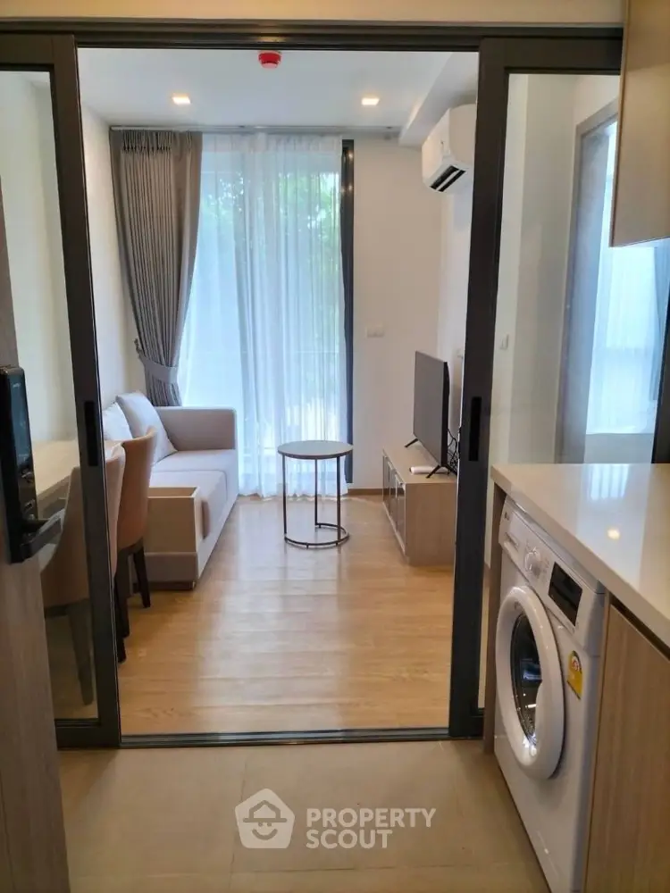 Modern apartment interior with open living room and kitchen featuring washing machine and sleek furniture.