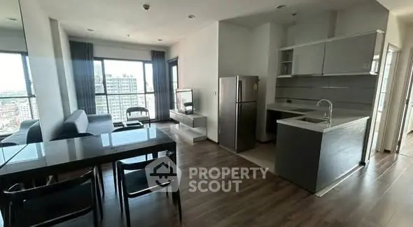 Modern open-layout living room with kitchen and city view, featuring sleek furniture and large windows.