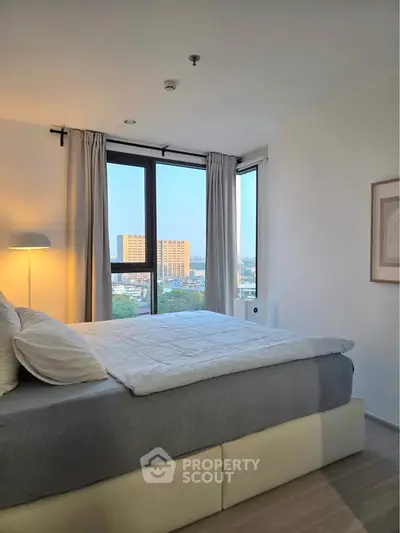 Bright and cozy bedroom with large windows offering a stunning city view, perfect for relaxation and comfort.