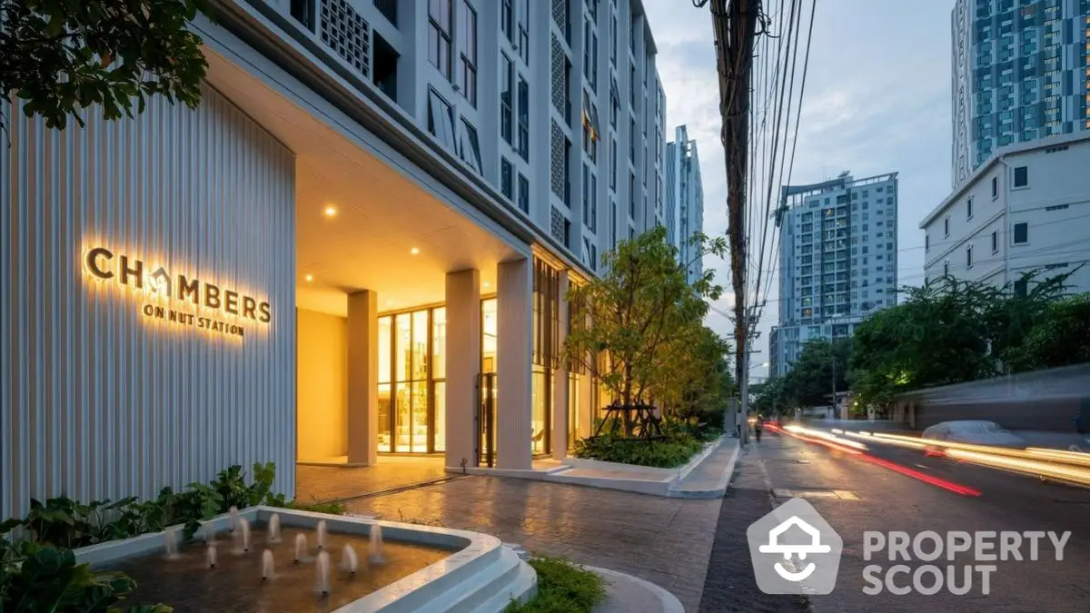 Modern apartment building entrance with illuminated signage and street view at dusk.