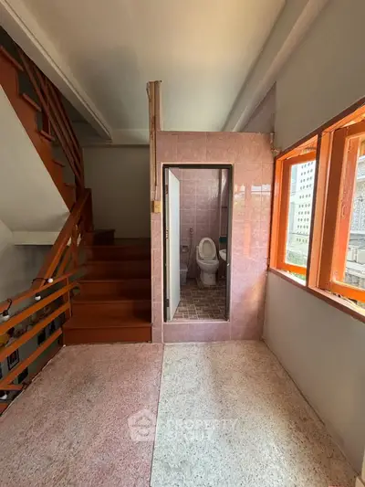 Unique duplex with staircase and compact bathroom, featuring large windows for natural light.