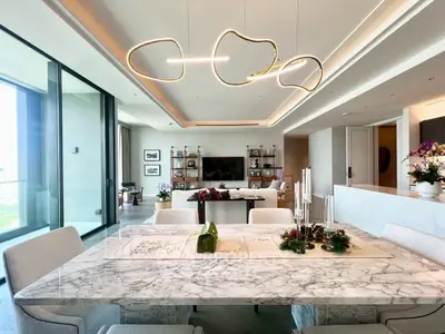 Luxurious open-plan living and dining area with modern lighting and marble table, featuring floor-to-ceiling windows.