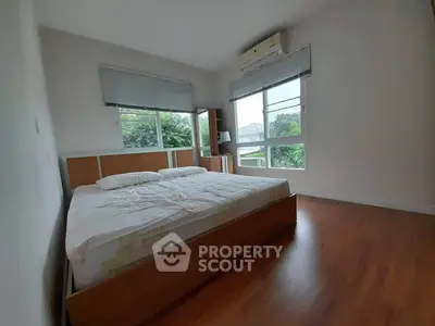 Spacious bedroom with large windows and wooden flooring, featuring a cozy bed and air conditioning.