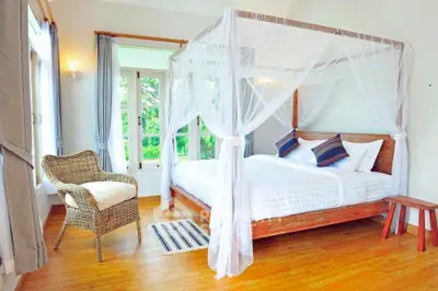 Charming bedroom with canopy bed and wicker chair, featuring large windows and natural light.