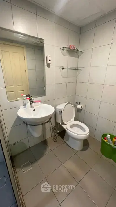 Modern bathroom with sleek fixtures and tiled walls, featuring a pedestal sink and toilet.