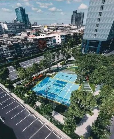 Aerial view of modern urban tennis court surrounded by lush greenery and cityscape.