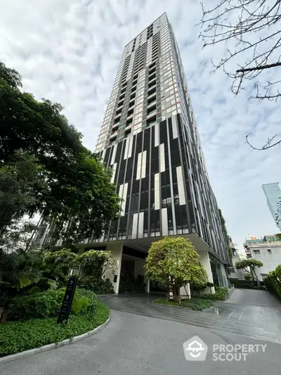 Modern high-rise building with sleek facade and lush greenery entrance