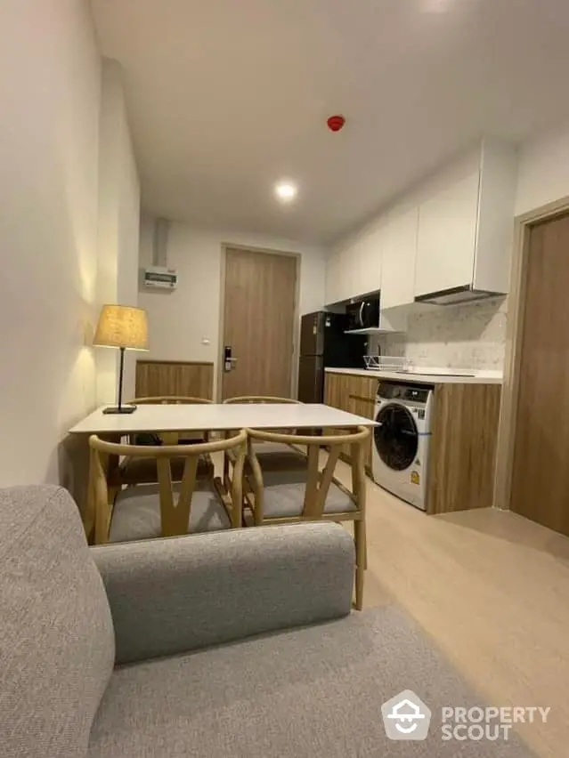 Cozy modern studio apartment with integrated living space, featuring a comfortable sofa, a compact dining set, and a fully equipped kitchen with a built-in oven and washing machine.