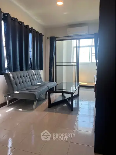 Modern living room with sleek sofa and glass coffee table, featuring large windows and elegant curtains.