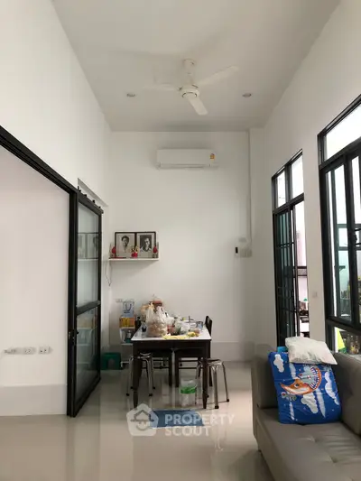 Modern living room with high ceiling and large windows, featuring a cozy dining area.