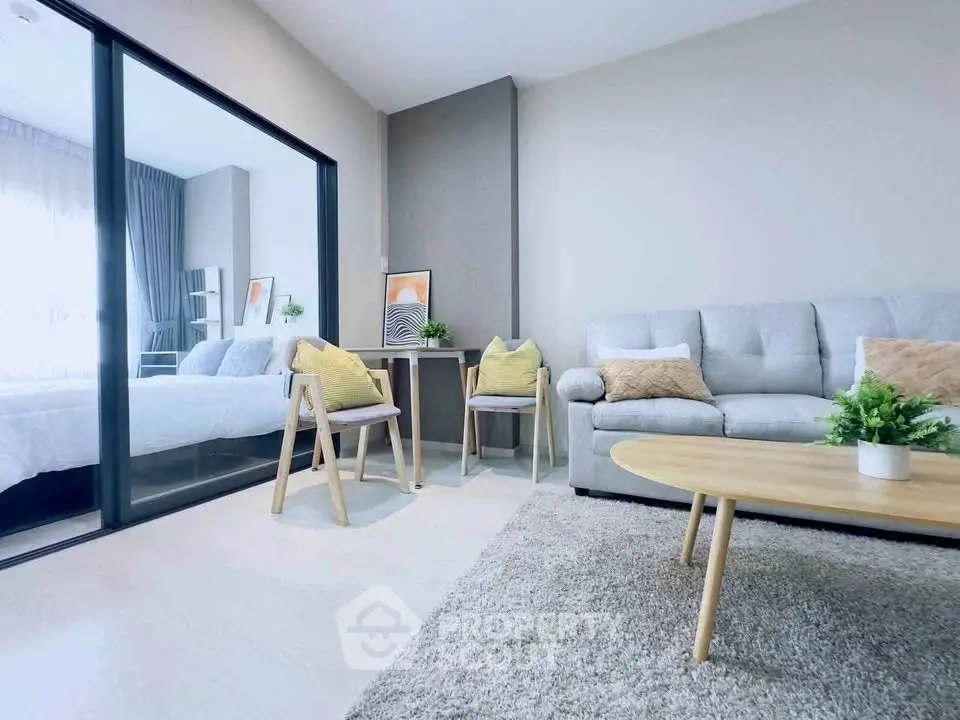 Modern living room with cozy sofa, stylish decor, and view into a bright bedroom through glass doors.