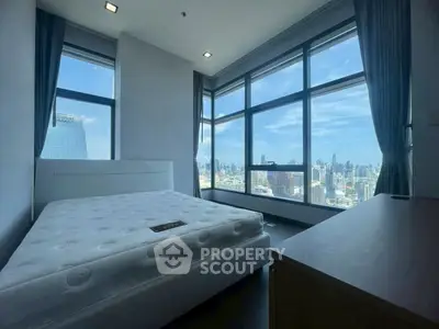 Spacious bedroom with panoramic city views and large windows in a modern high-rise apartment.