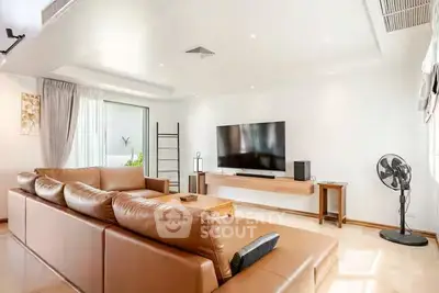Spacious modern living room with leather sofa and large TV, perfect for relaxation.