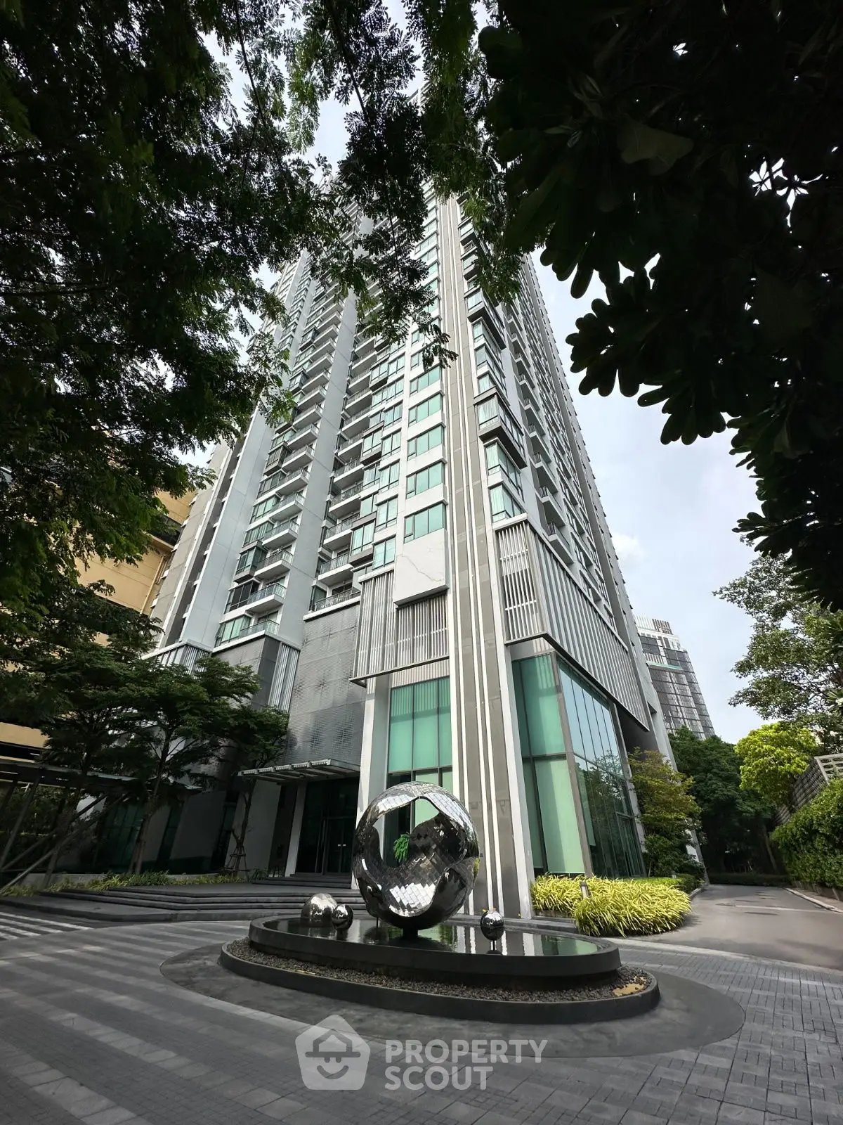 Modern high-rise building with sleek architecture and lush greenery in urban setting.