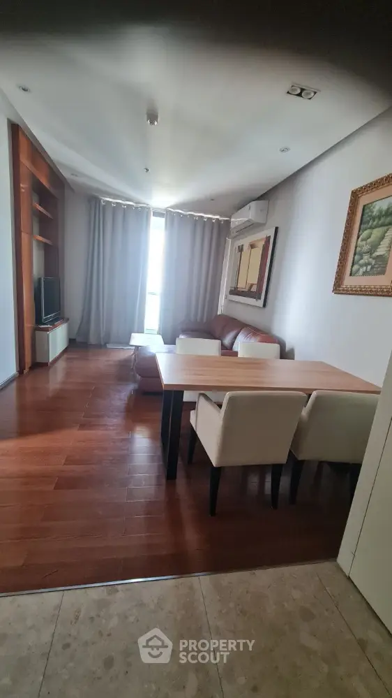 Modern living room with wooden flooring, cozy seating, and natural light from large window.