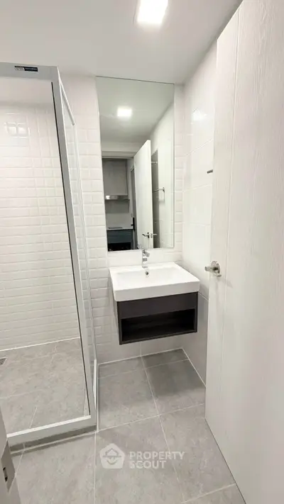 Modern bathroom with sleek design, featuring a large mirror, white sink, and glass shower enclosure.