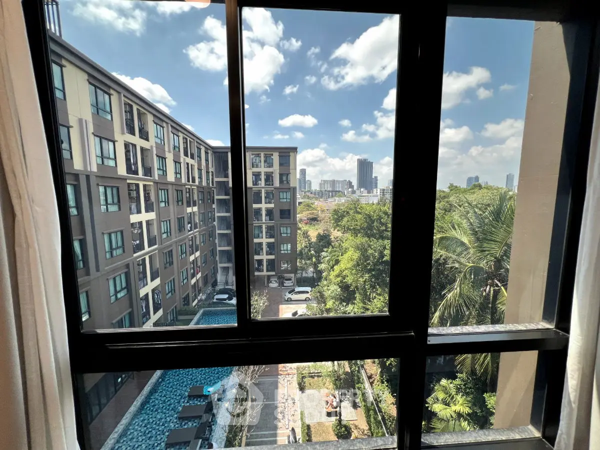 Stunning city view from high-rise apartment window overlooking modern buildings and lush greenery.
