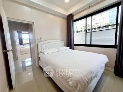 Cozy bedroom with large window and elegant white bedding in modern apartment.