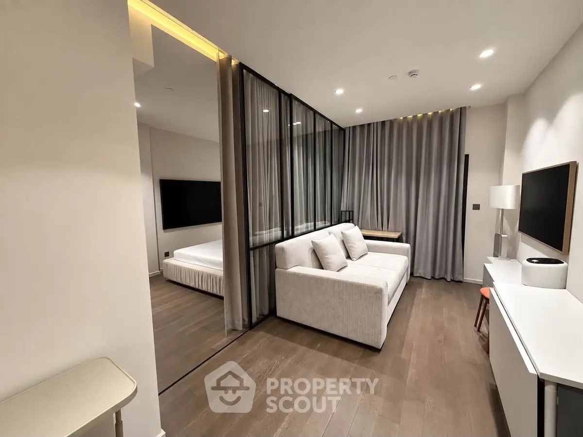 Modern living room with sleek design and partitioned bedroom area, featuring elegant lighting and contemporary furniture.