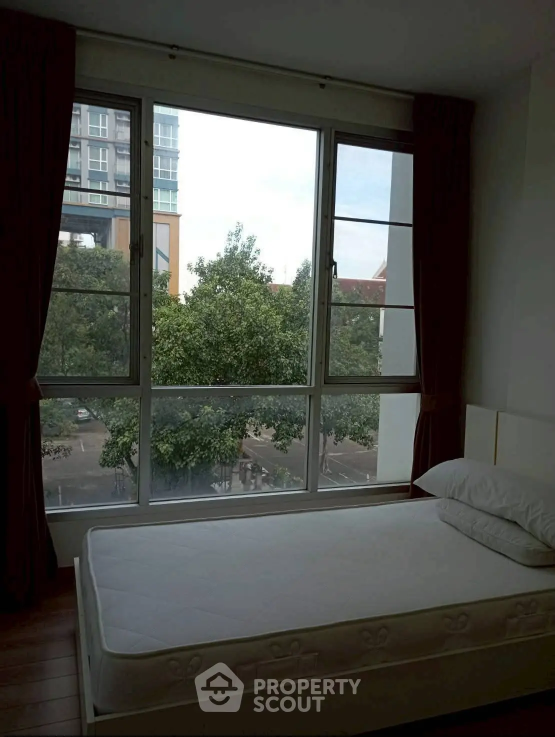 Cozy bedroom with large window offering a serene view of trees and cityscape.