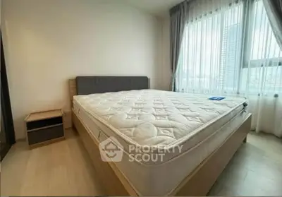 Spacious bedroom with large window and modern furnishings in a high-rise apartment.