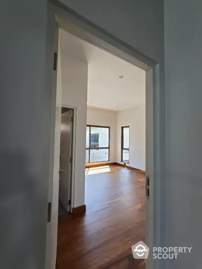 Spacious sunlit room with wooden flooring and large windows in modern home.