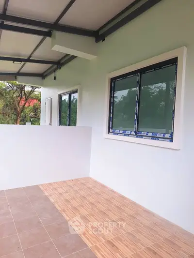 Spacious balcony with tiled flooring and large windows overlooking greenery.