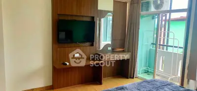 Modern bedroom with TV and balcony access, featuring stylish wooden furniture and natural light.