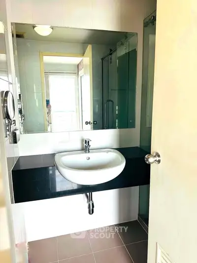 Modern bathroom with sleek sink and large mirror, featuring a glass shower enclosure.