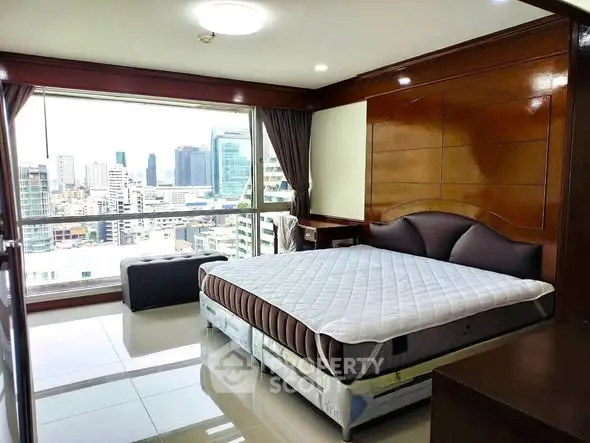 Spacious bedroom with city view and modern furnishings in high-rise apartment.
