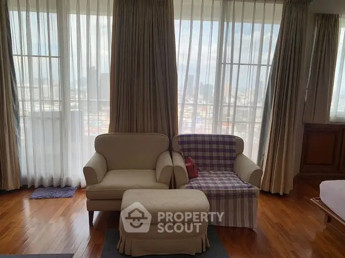 Spacious living room with large windows draped in elegant curtains, offering ample natural light and a cozy seating area.