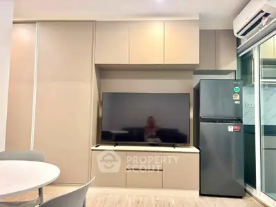 Modern living room with sleek cabinetry, flat-screen TV, and stainless steel fridge in a stylish apartment.