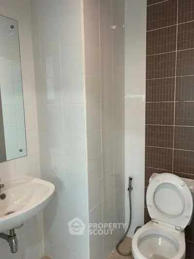 Modern bathroom with white and brown tiled walls, featuring a pedestal sink, toilet, and a large mirror reflecting the interior.