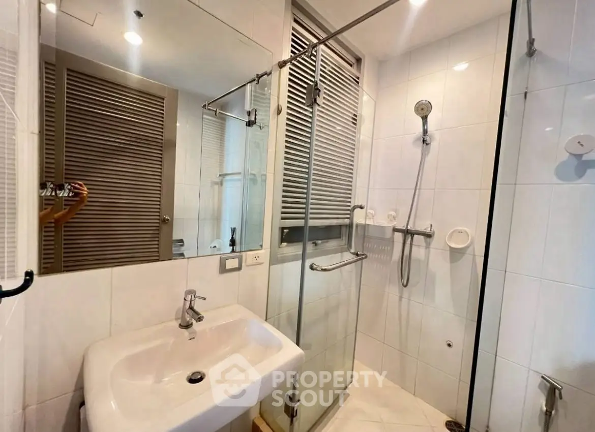 Modern bathroom with glass shower and sleek white sink in contemporary apartment.